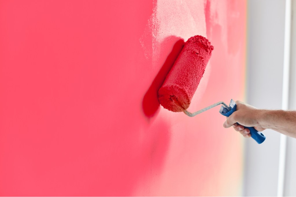 Man's hand painting a wall pink with a paint roller