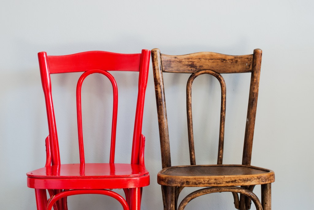 Two wooden chairs next to each other: one is painted red and one is natural wood.