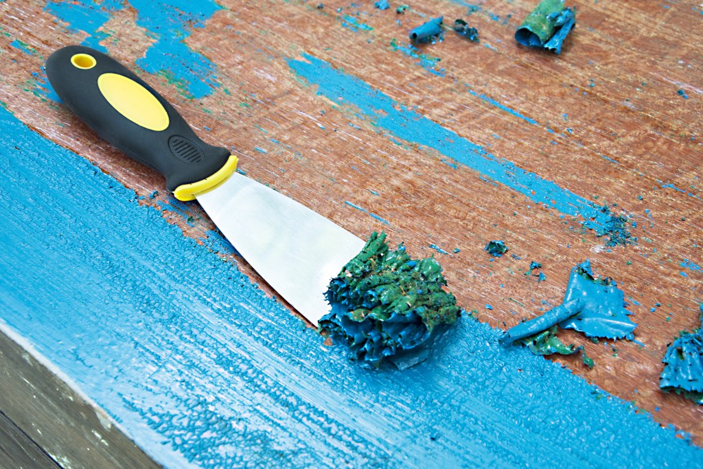 Metal paint scraper scraping blue paint off wood