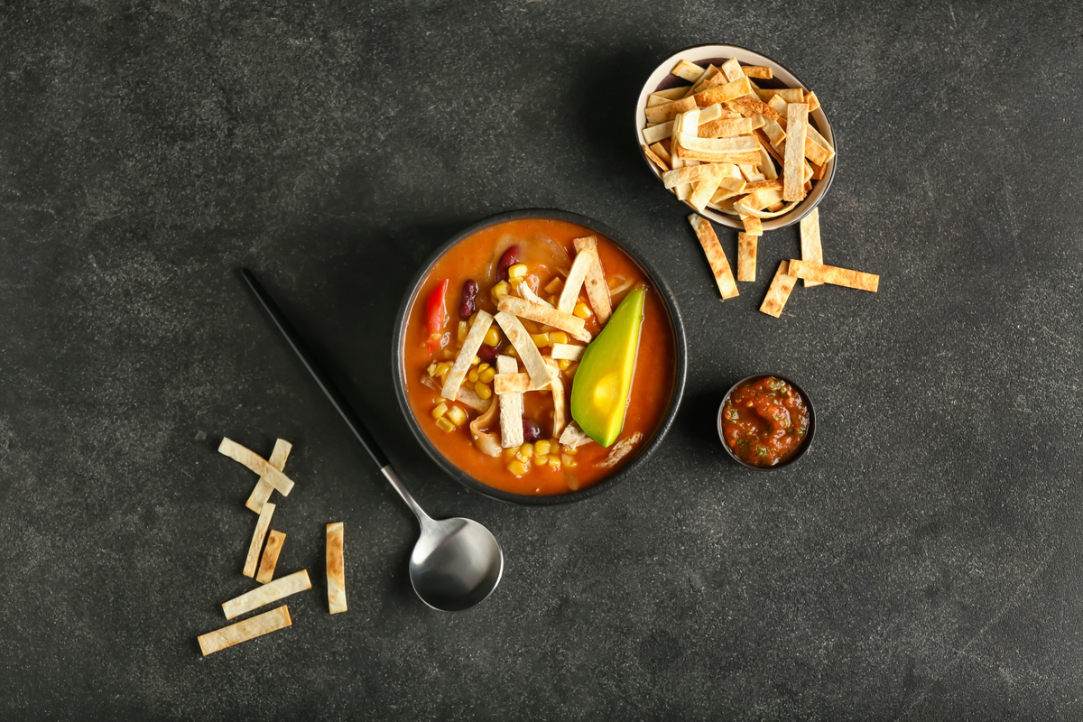 A bowl of chicken tortilla soup and some bowls of garnishes.