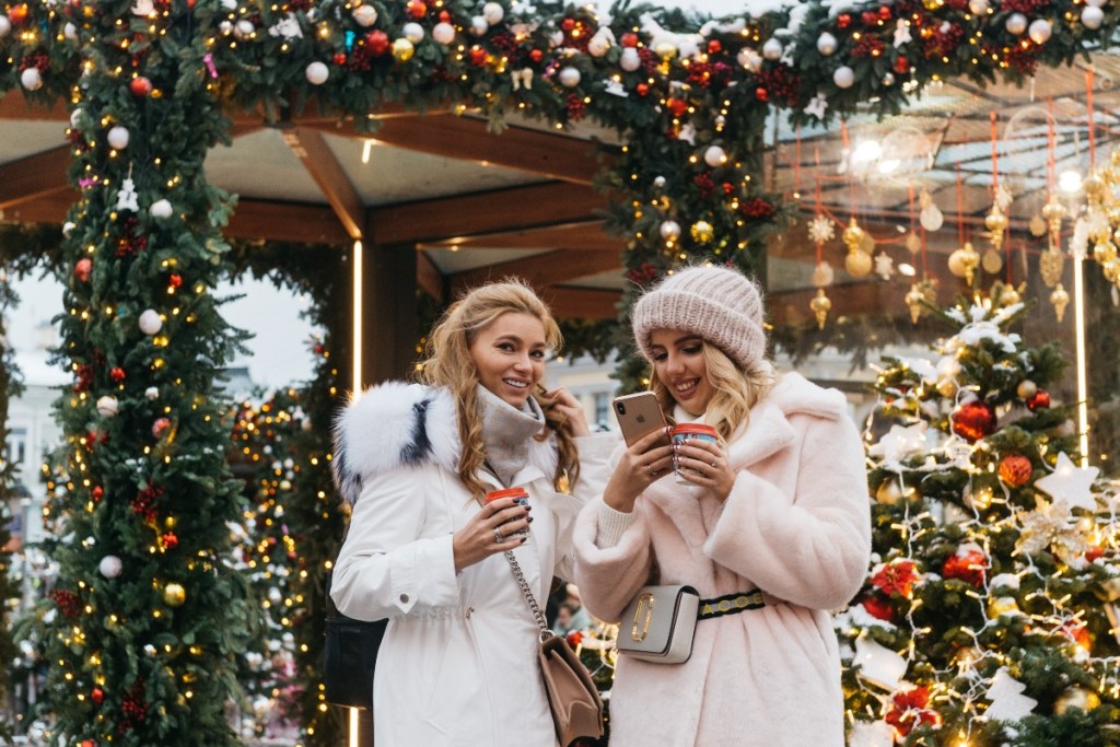 Two women holiday shopping and one is looking at her phone