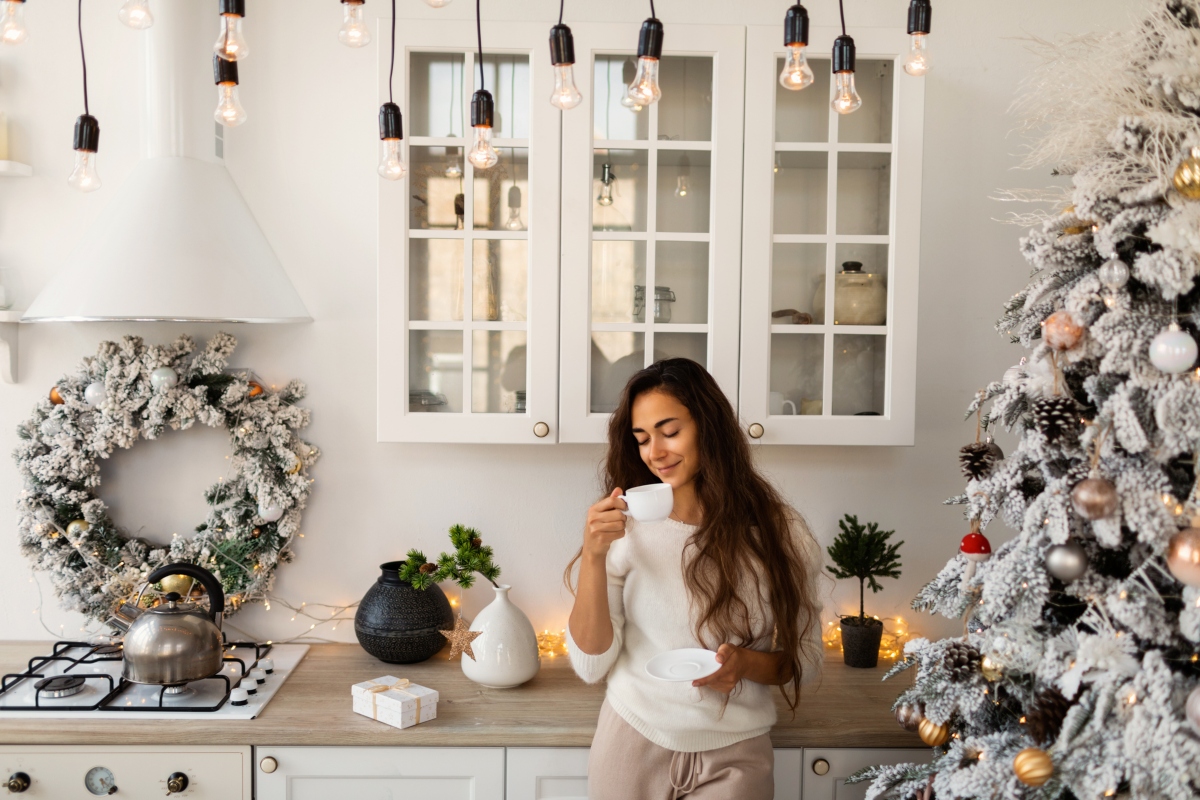 Woman drinking coffee in rustic kitchen with a Christmas tree