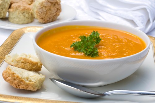 Carrot soup in a white bowl with a side of bread