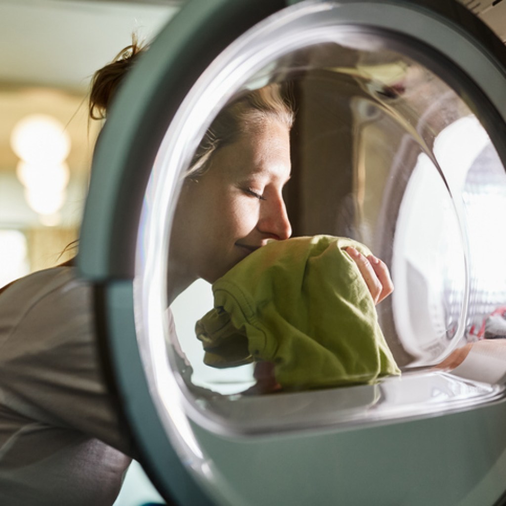 Woman smelling freshly dried clothes in front of dryer