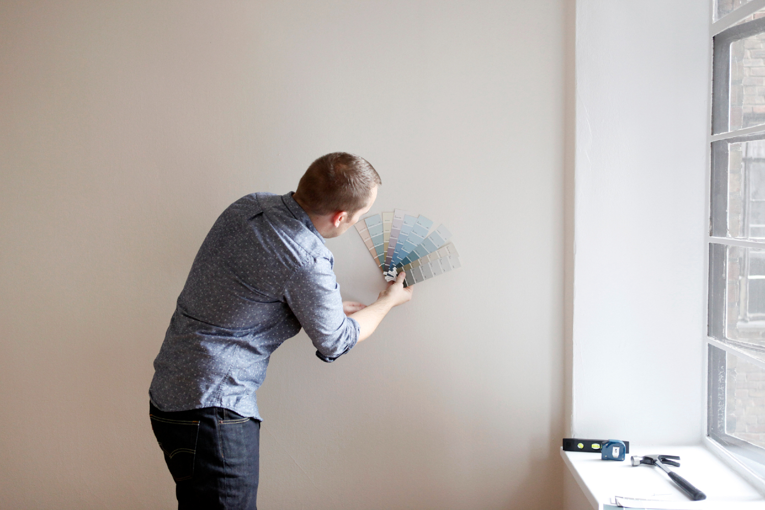 Man comparing paint swatches to greige walls.