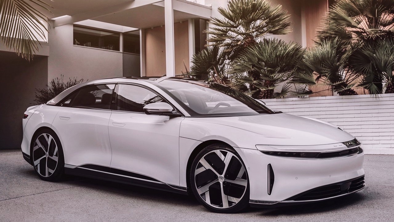 Three quarters front view of a white Lucid Air parked in a modern house's driveway.