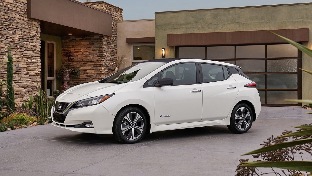 Three quarters front view of a Nissan Leaf parked in a modern house's driveway.