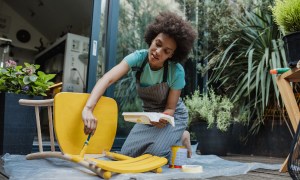 Woman painting chair yellow on deck outside.