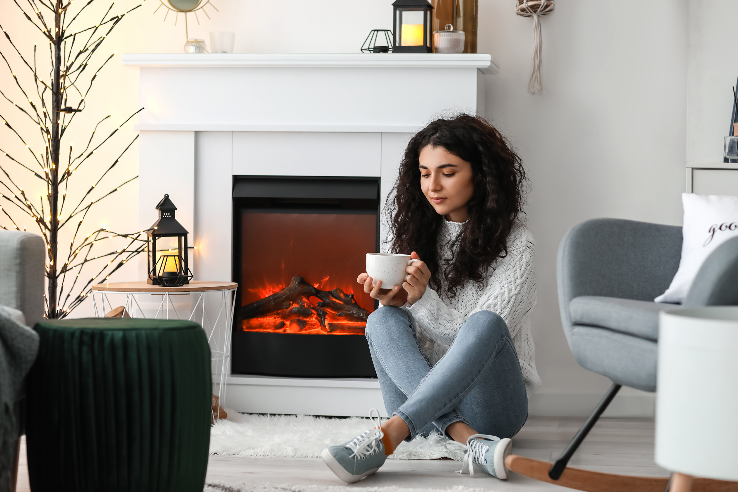 Woman sitting by electric fireplace with mug