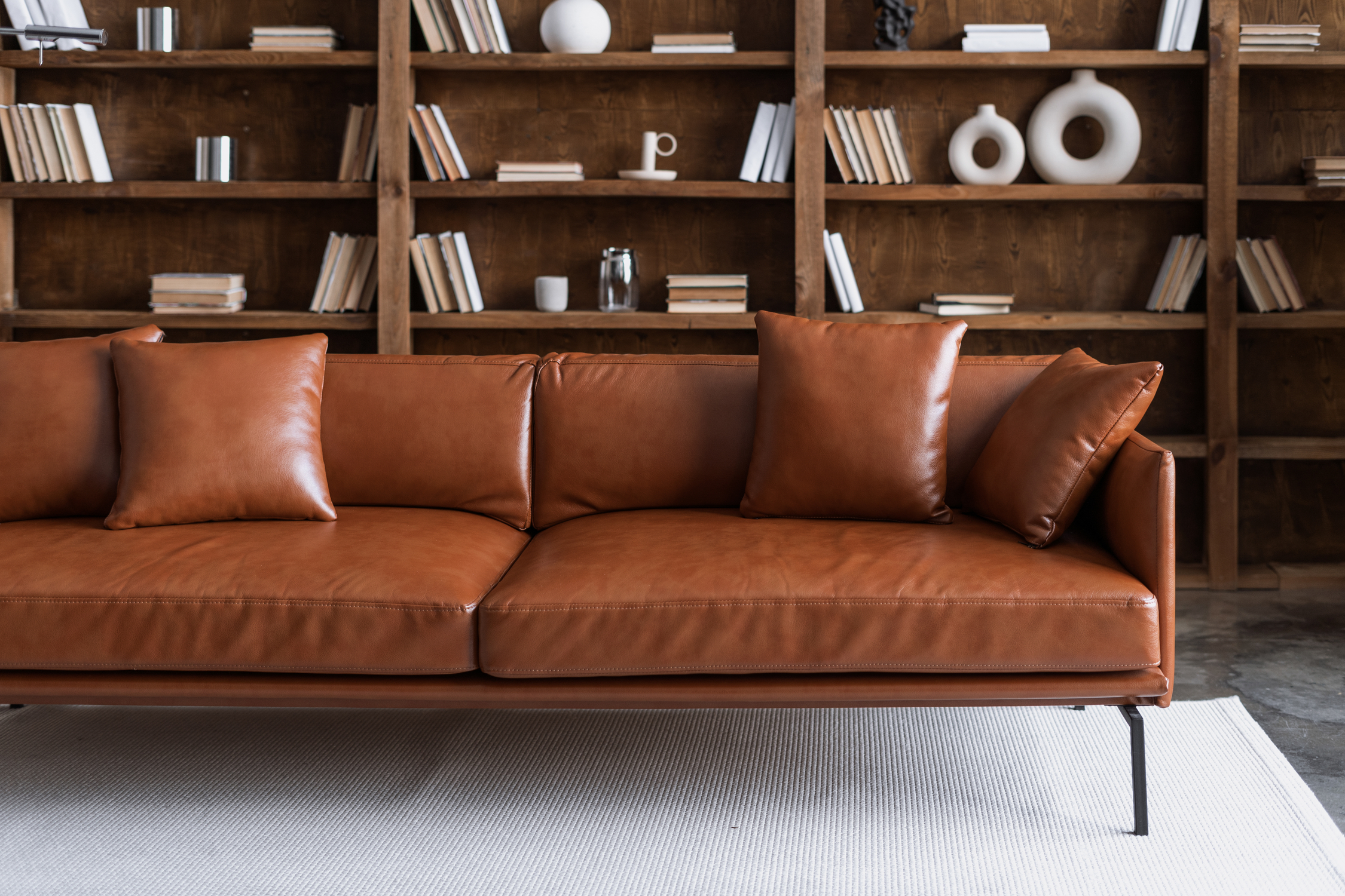 Brown leather couch in front of wood bookshelf