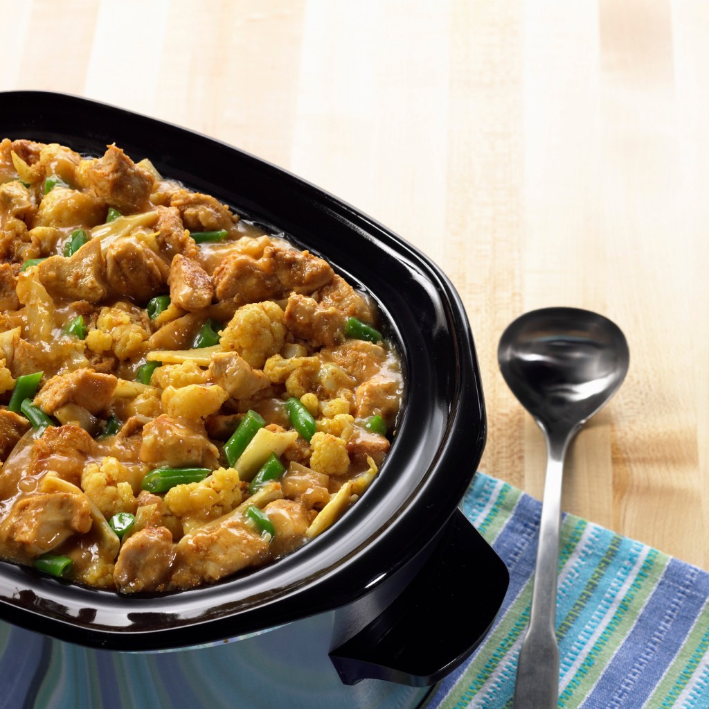 Crockpot with chicken dinner inside beside spoon