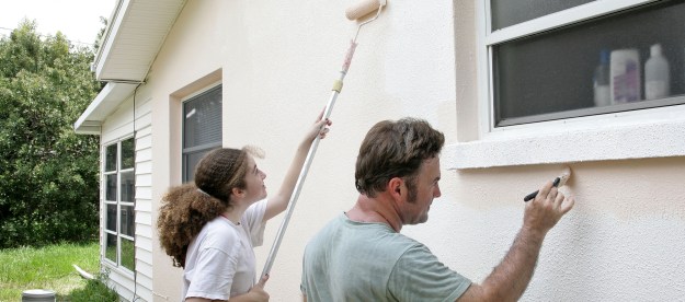 Father and daughter painting exterior of house