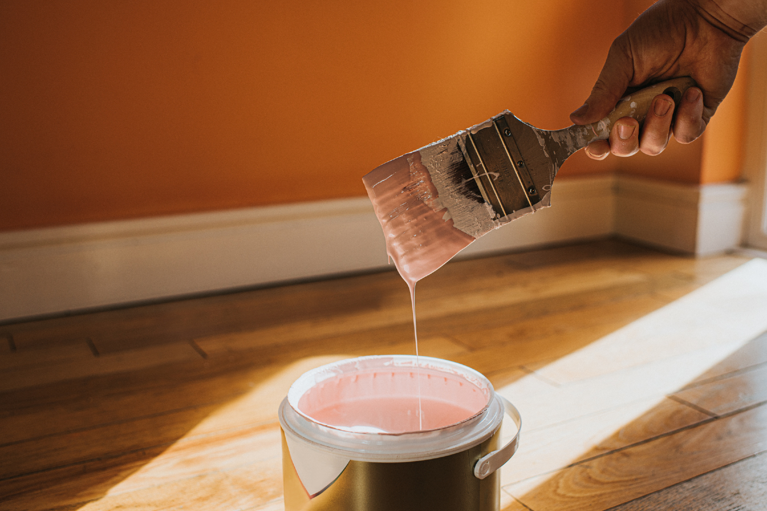Hand holding paint brush over paint can.