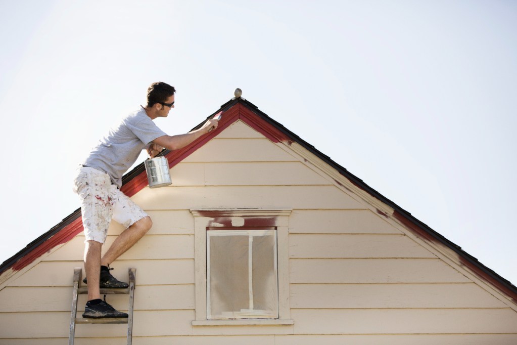 Guy on ladder painting exterior of house.