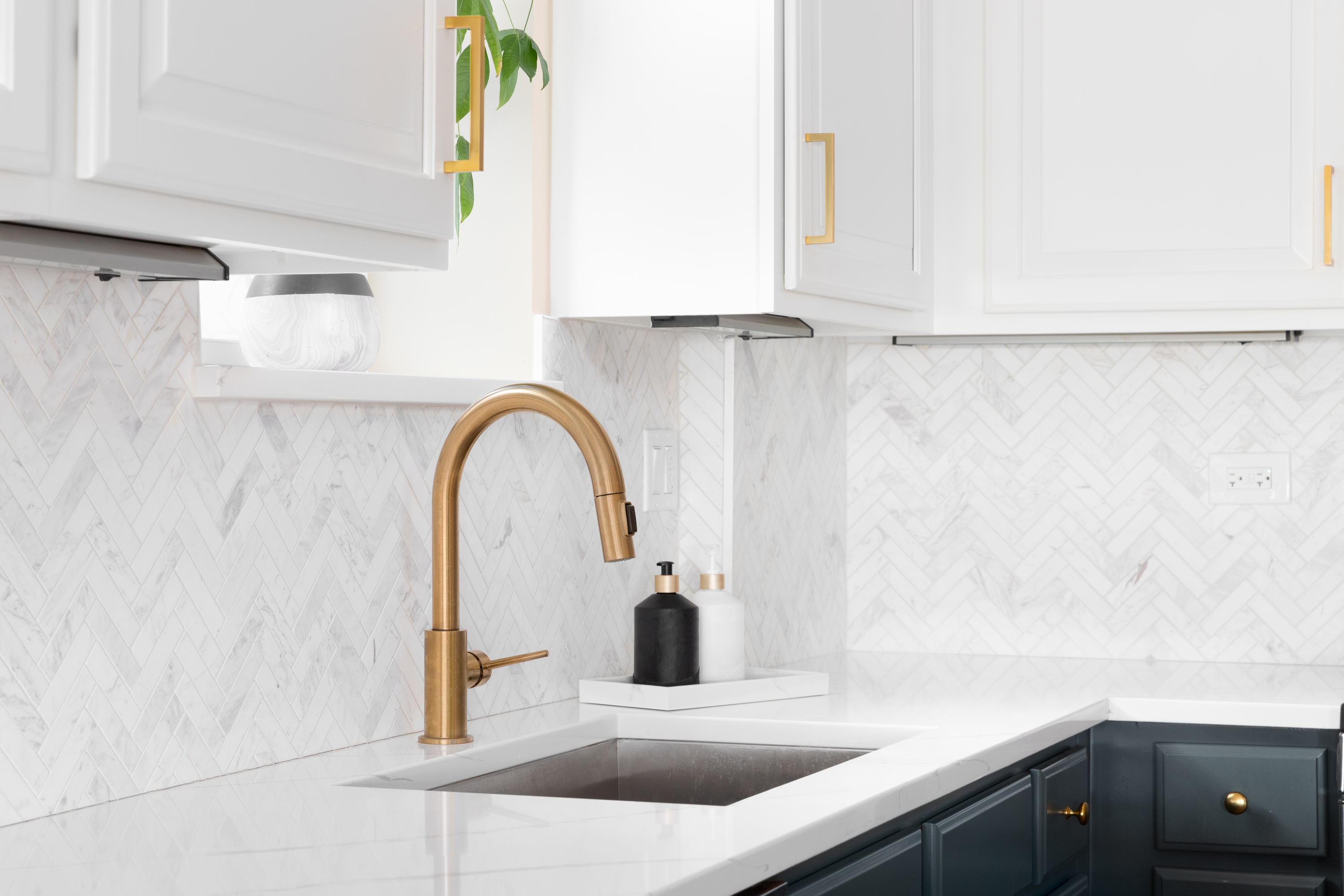 Gold kitchen sink faucet with herringbone backsplash and marble countertop