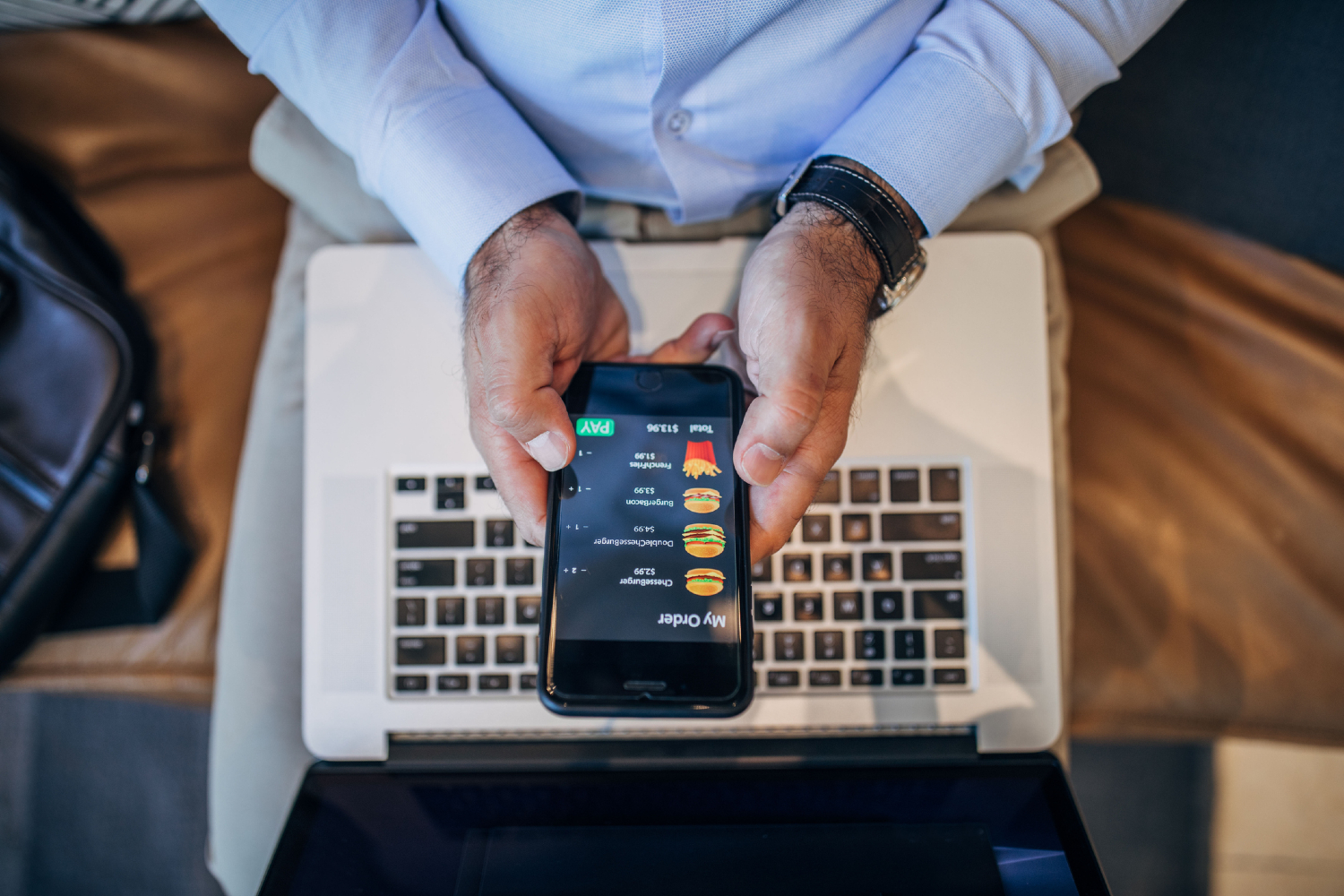 Person using fast food delivery app on phone with laptop on lap.
