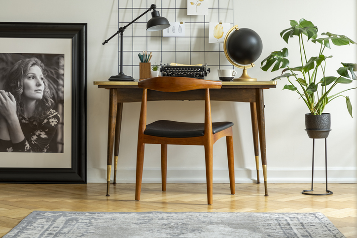 Midcentury modern chair with leather seat by a desk with an industrial lamp and a retro typewriter in a white home office interior