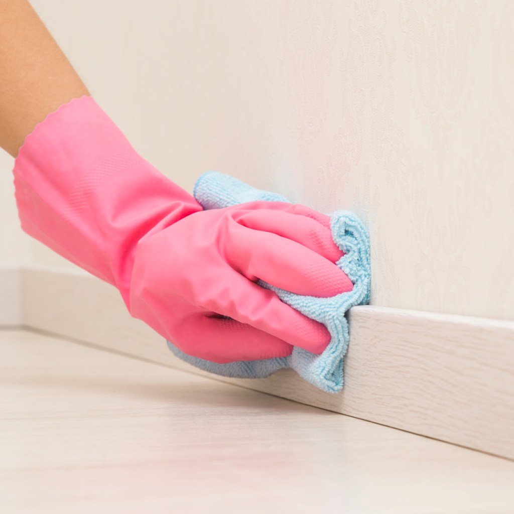 Pink gloved hand wiping baseboards