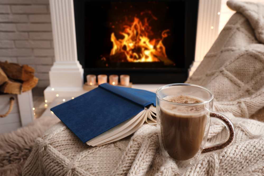 Cozy by fireplace with book, hot chocolate, and blanket