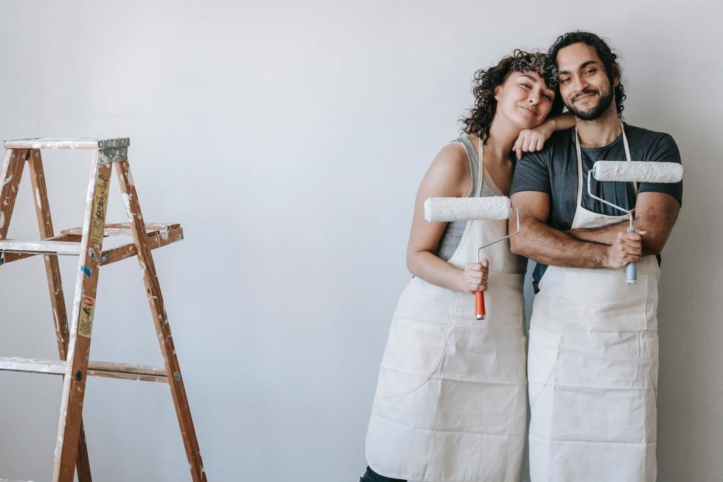 Couple posing with paint rollers in front of painted white wall