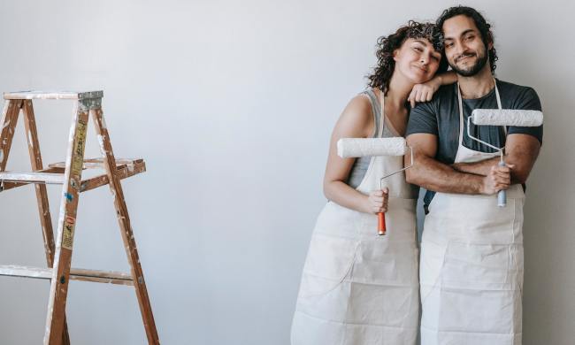 Couple posing with paint rollers in front of painted white wall