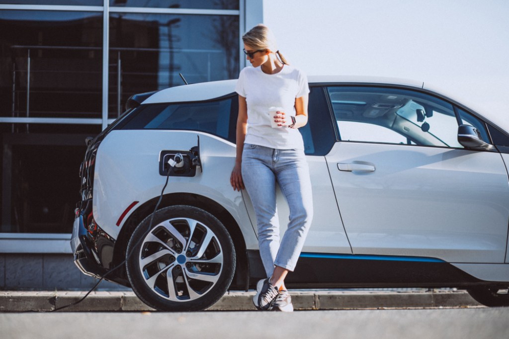 Woman holding coffee next to charging electric vehicle