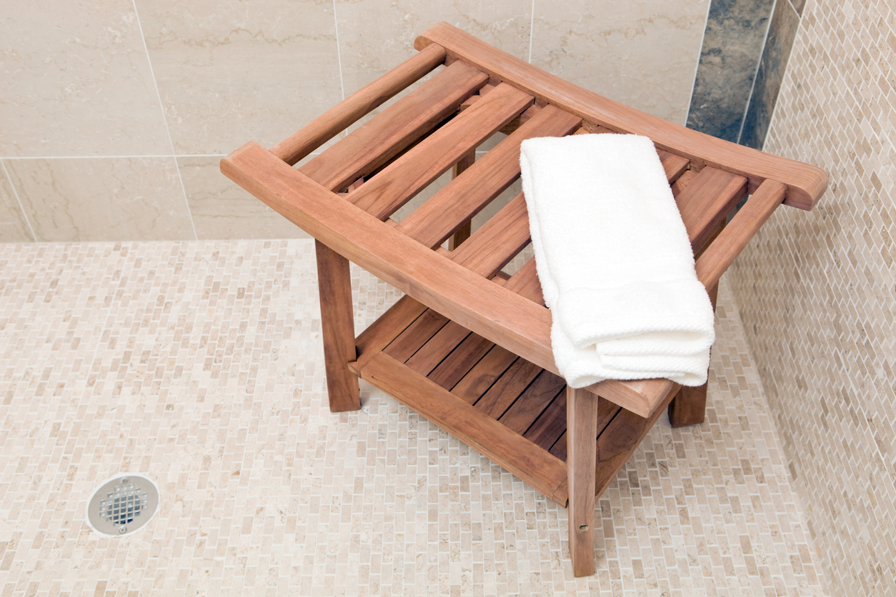 A wooden shower bench with a hand towel on top