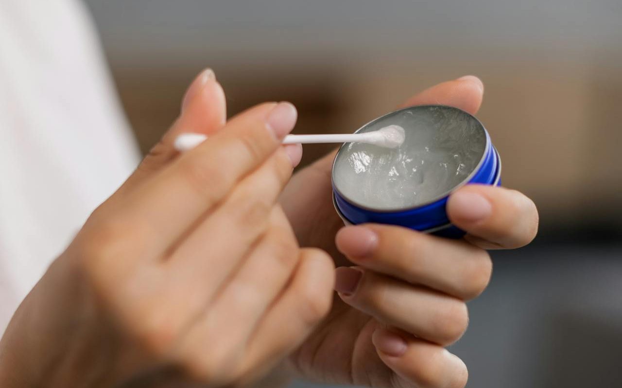 woman using cotton swab and tin of oil
