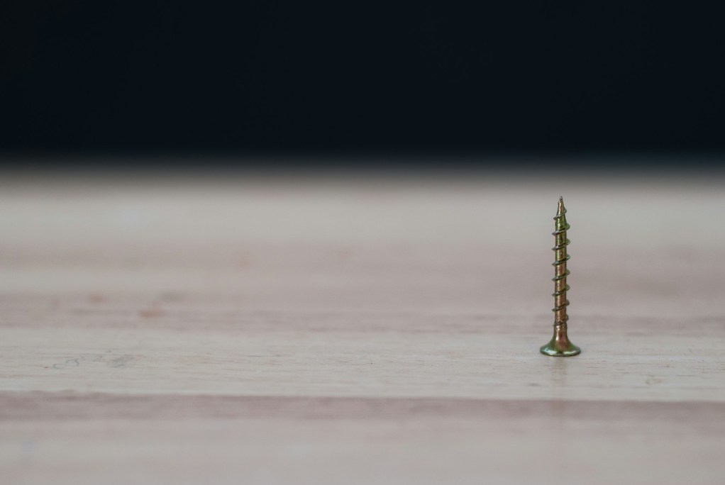 single screw pointed up on a wood surface