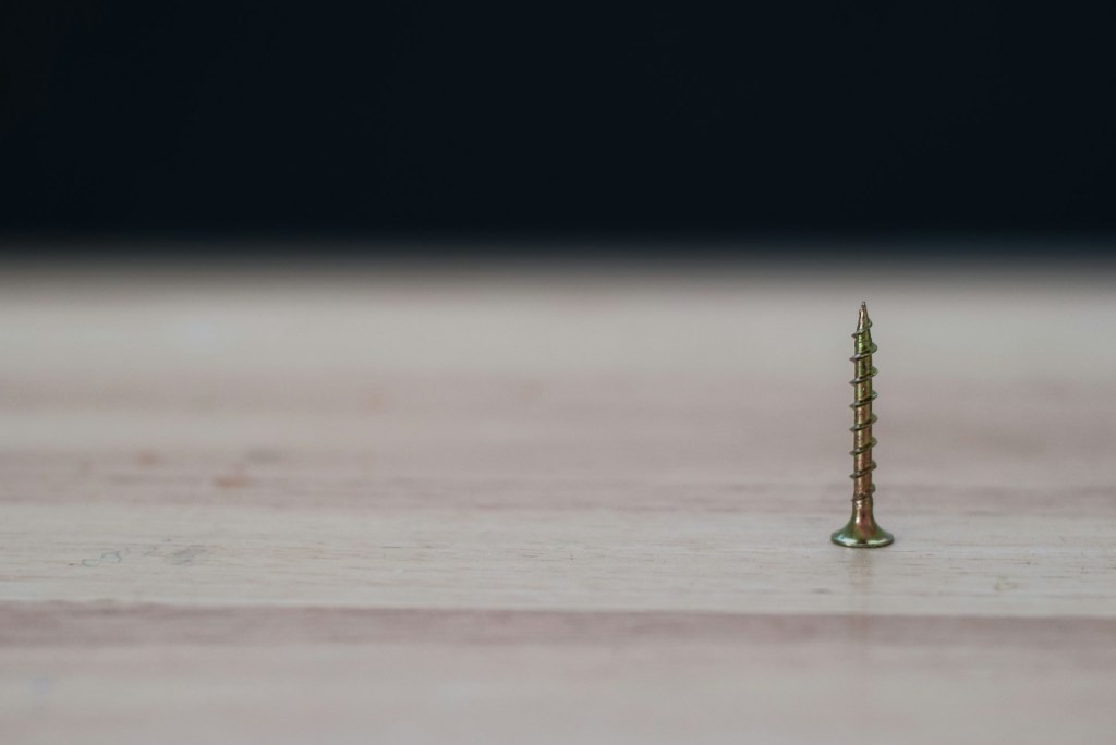 single screw pointed up on a wood surface