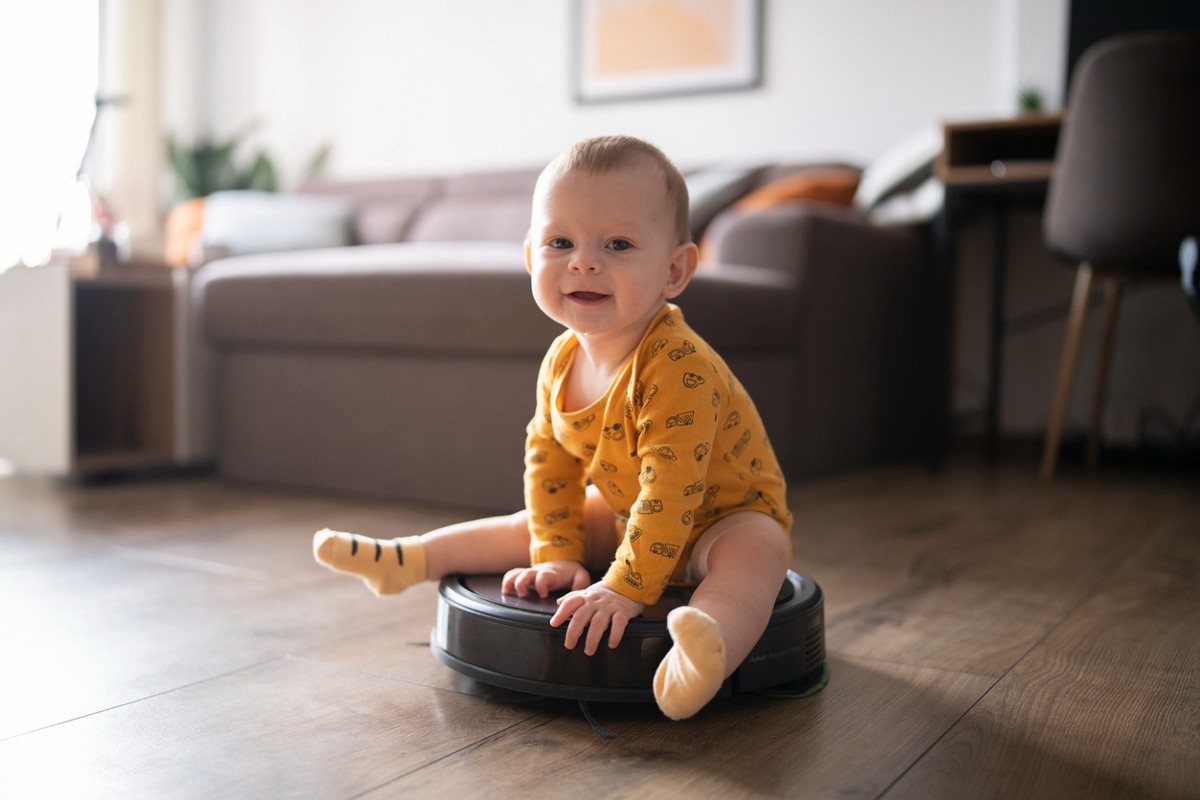 Cute and smiling little baby boy sitting on the robot vacuum cleaner and having a great time.