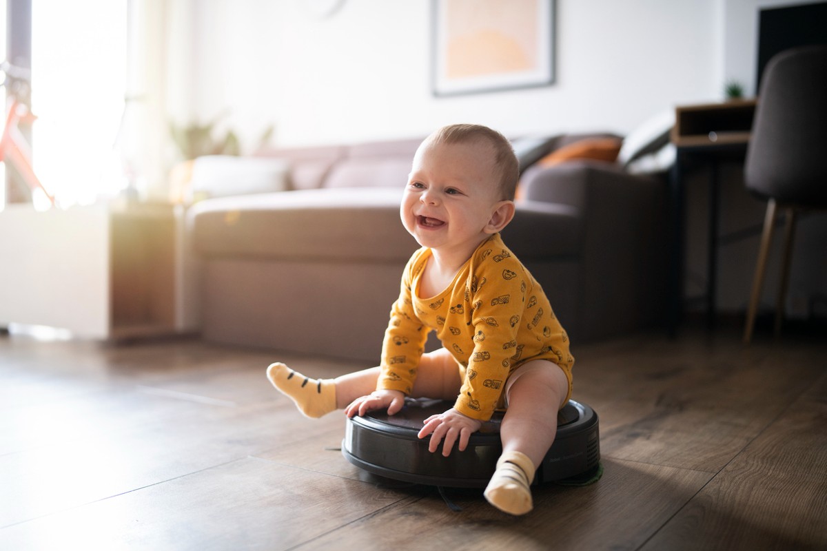 Cute and smiling little baby boy sitting on the robot vacuum cleaner and having a great time.