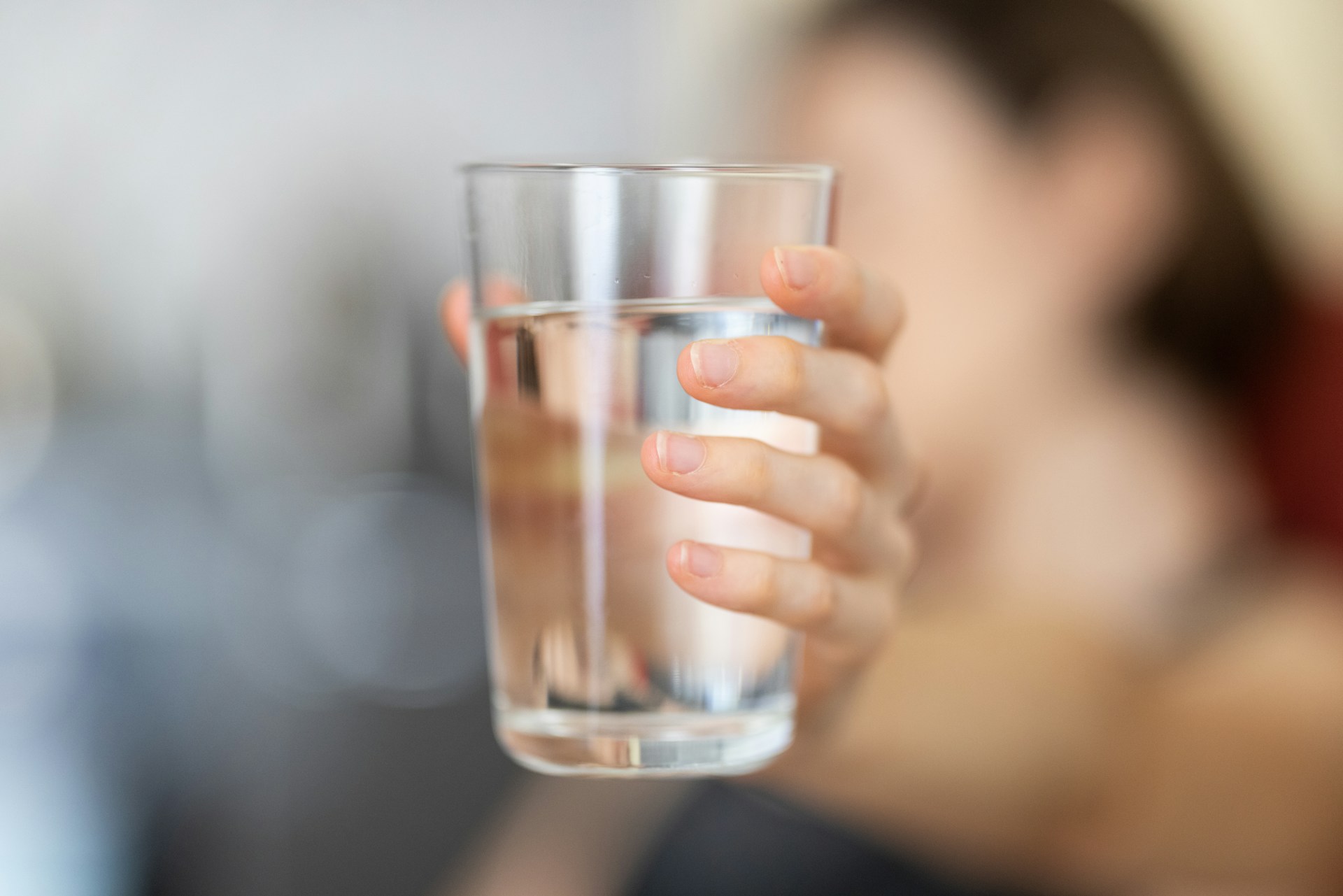 unfocused image of woman holding up clear water glass