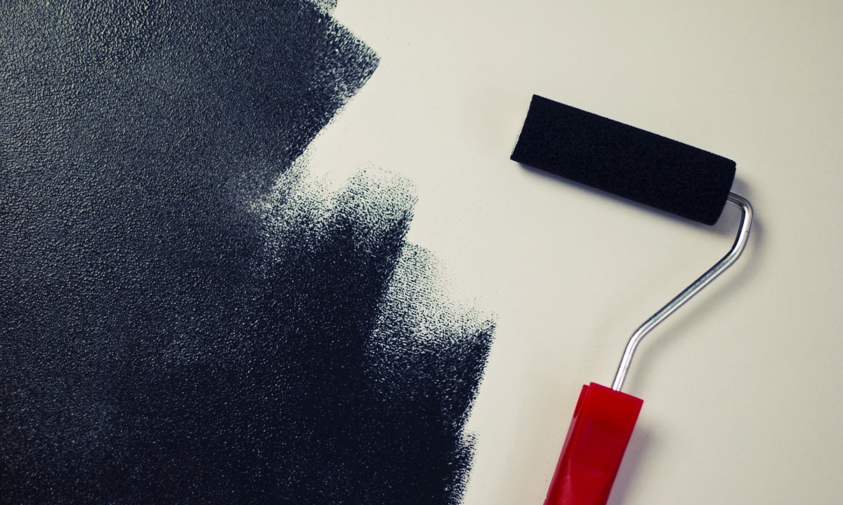 Black paint roller painting a white wall black