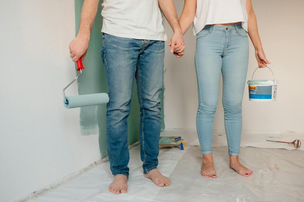 Man and woman in jeans holding hands with paint rollers