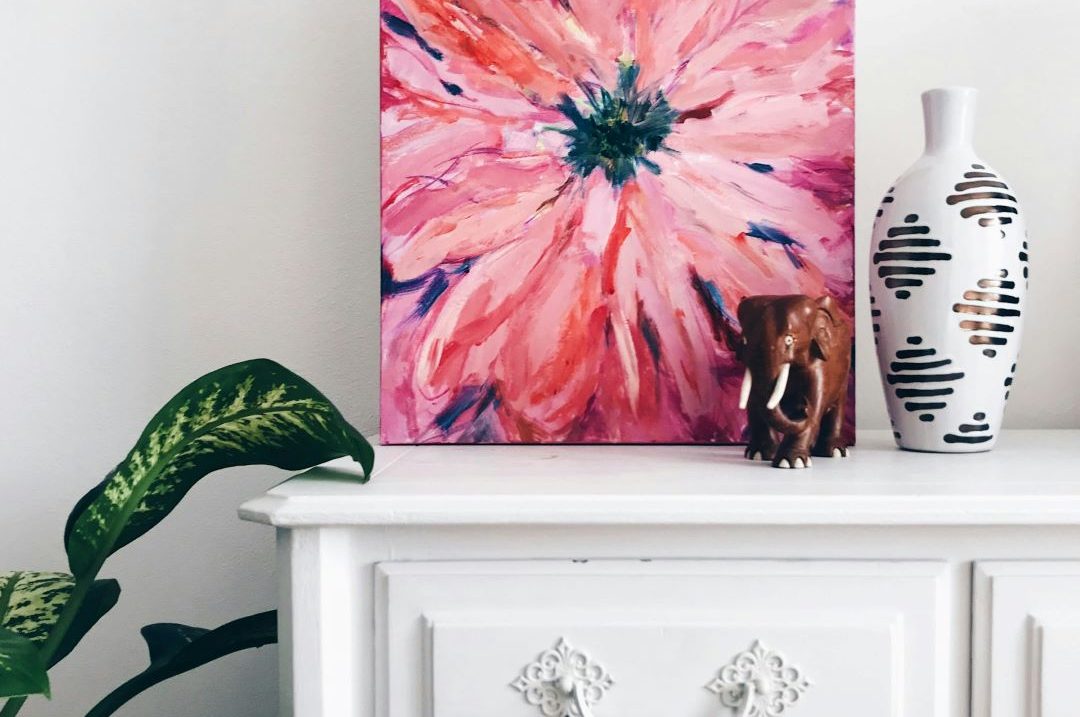 Painting of pink flower on white dresser next to dark green plant