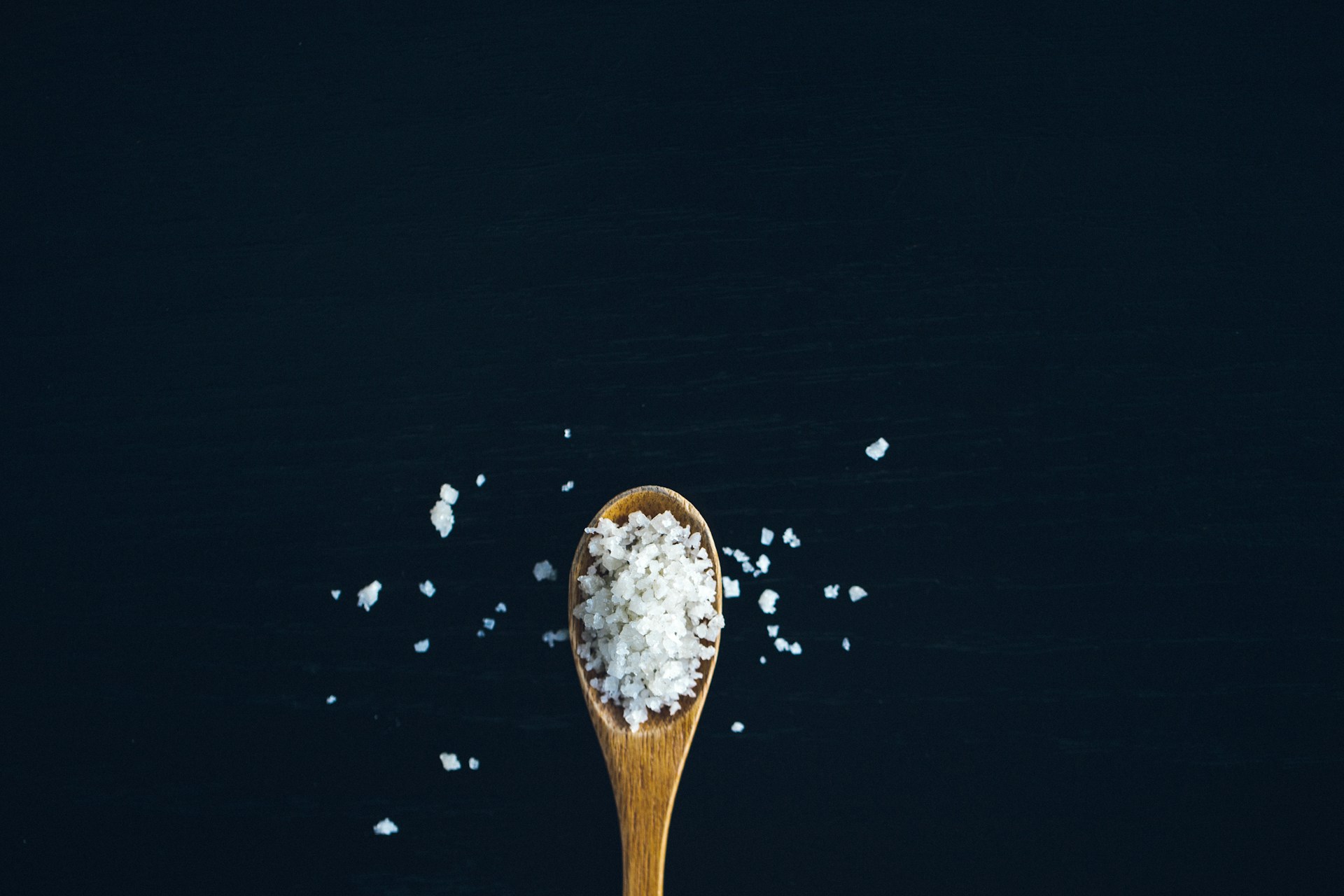 Coarse salt in a wooden spoon on a black surface