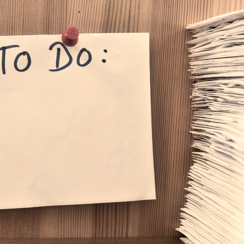 To do list tacked onto wood wall next to stack of papers