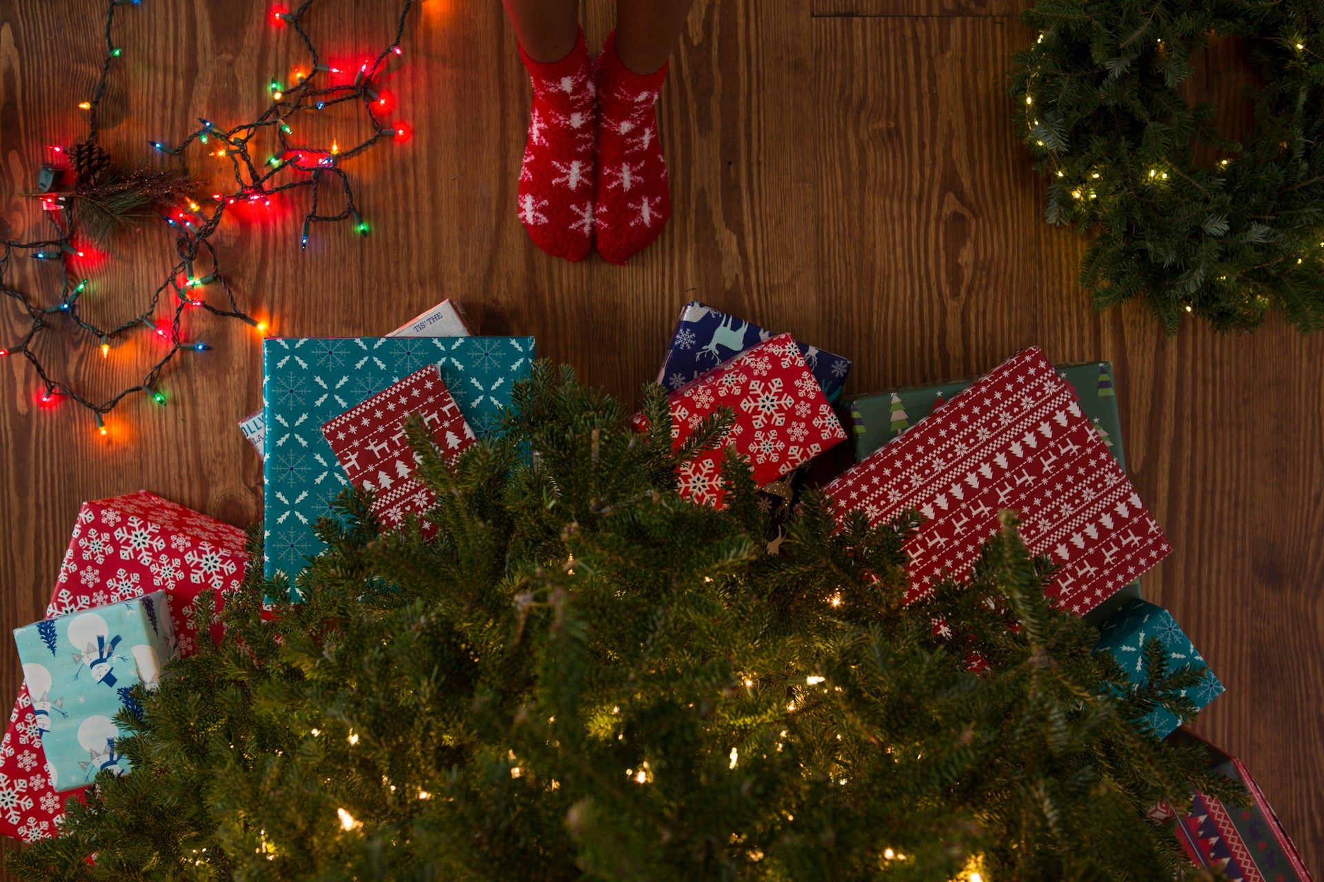 Person in christmas socks standing by lit tree and colored and white christmas lights