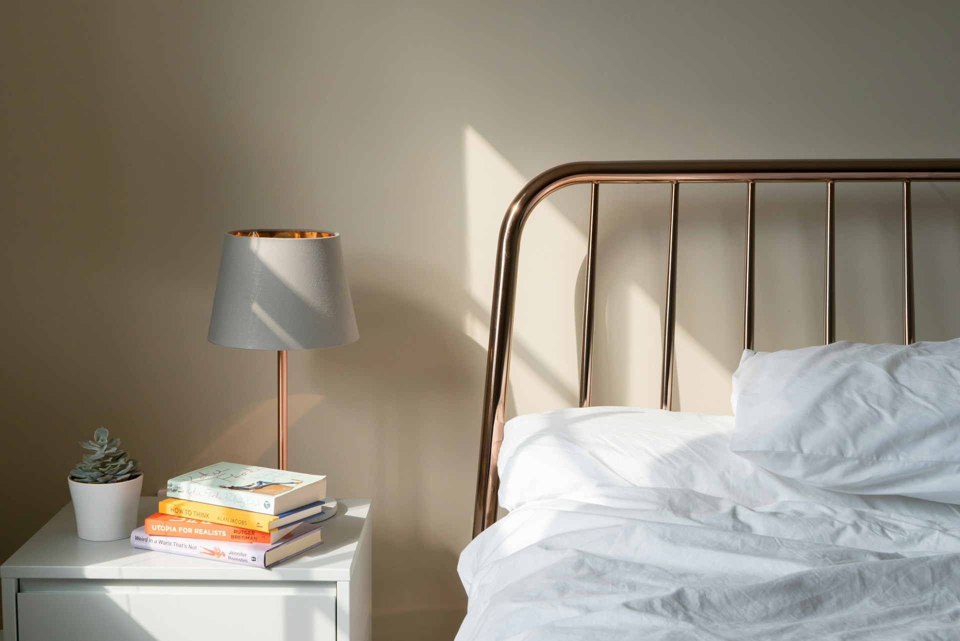 Messy white sheets on a modern bed next to night stand with books.