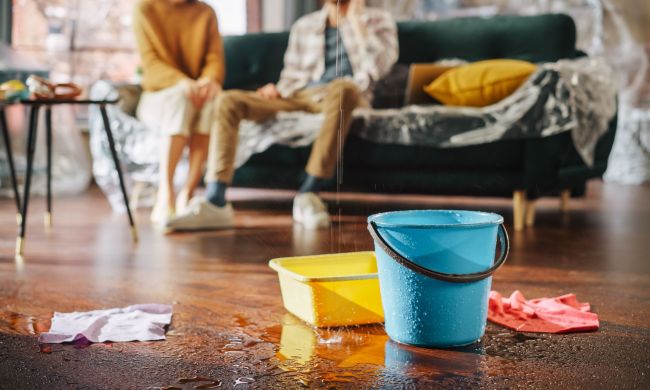 Couple sitting on couch covered in plastic with bucket catching roof leak. How to find a roof leak